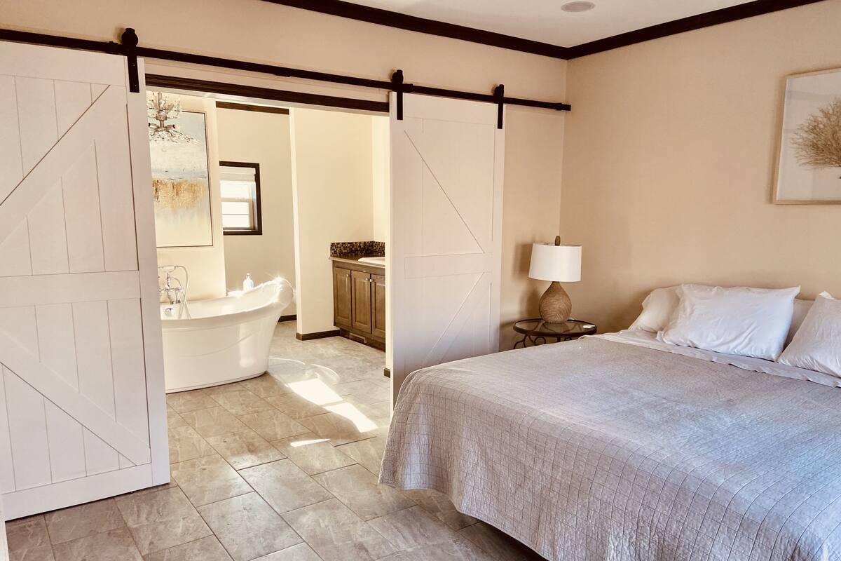 A bedroom with a large bed, a nightstand with a lamp, and a view into the bathroom.