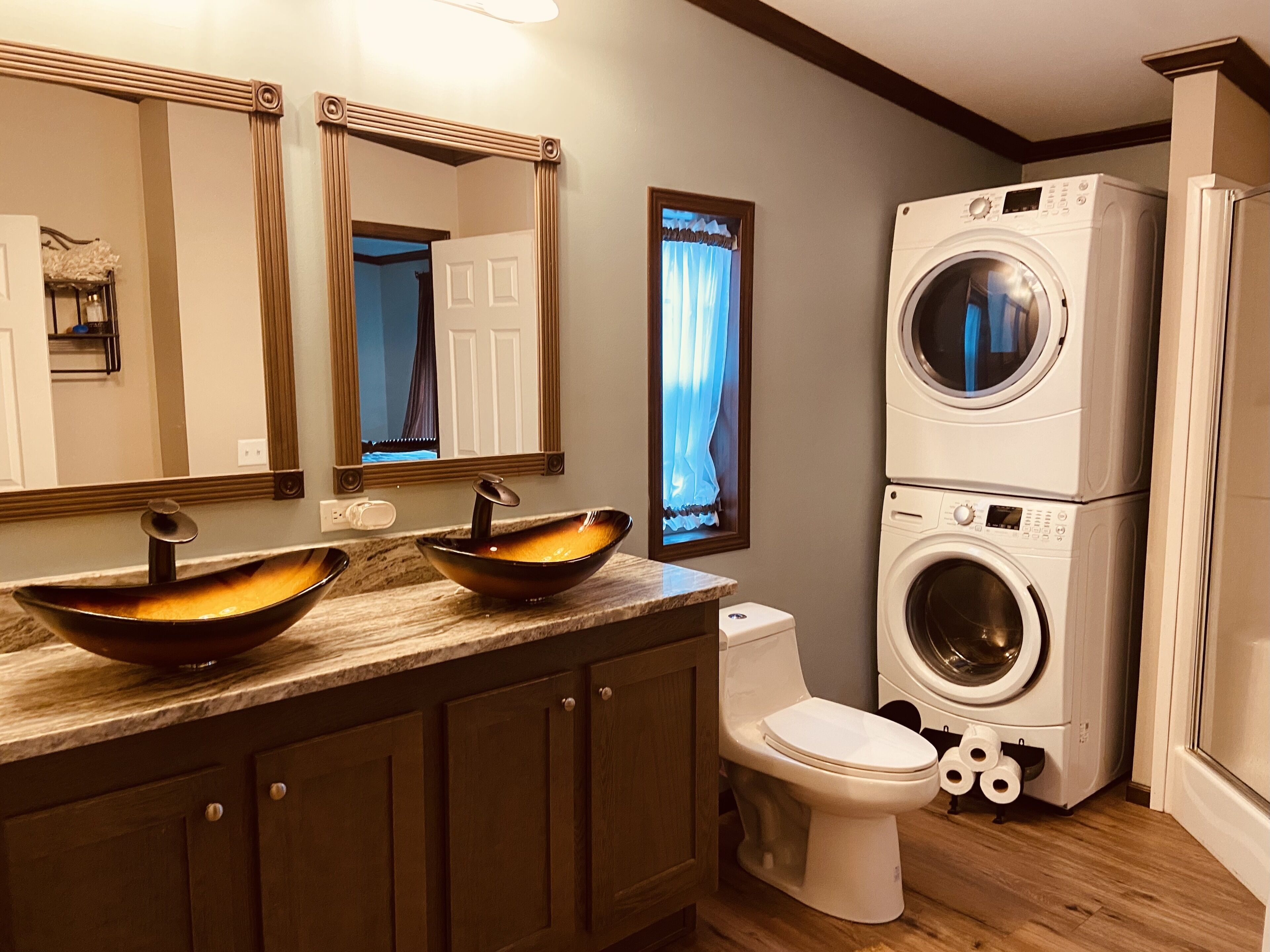 Baño con lavamanos doble, inodoro y lavadora y secadora apiladas.