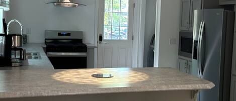 Une cuisine moderne dotée d’un îlot central, de tabourets de bar, d’appareils électroménagers en acier inoxydable et d’une fenêtre.
