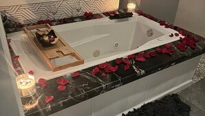 Un baño moderno con una bañera independiente, pétalos de rosa, velas y una bandeja de madera con una botella y un vaso.