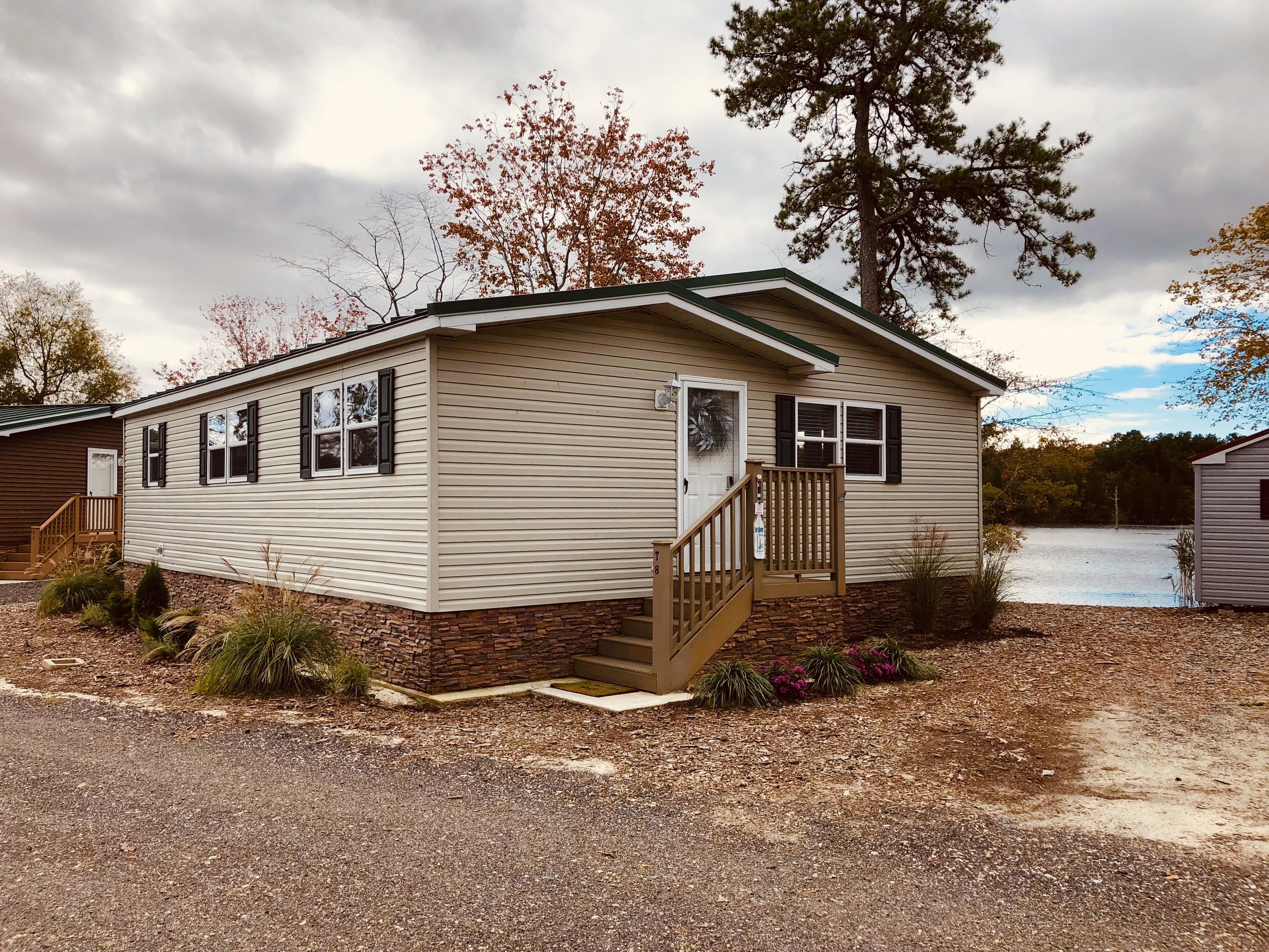 A single-story mobile home with a front porch, a small staircase, and a stone foundation.