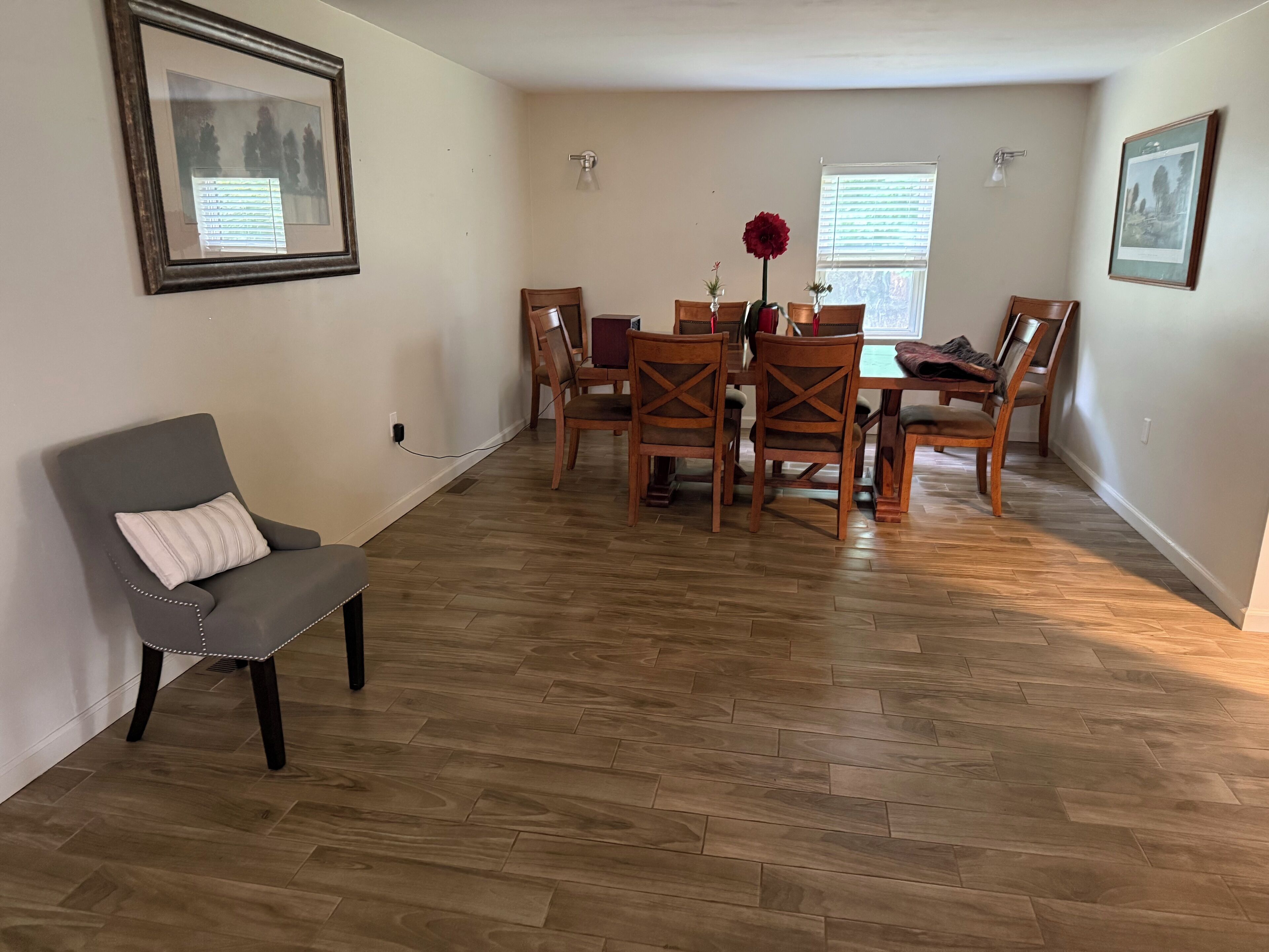 Un comedor con una mesa y sillas de madera, un sillón gris y dos cuadros en las paredes.