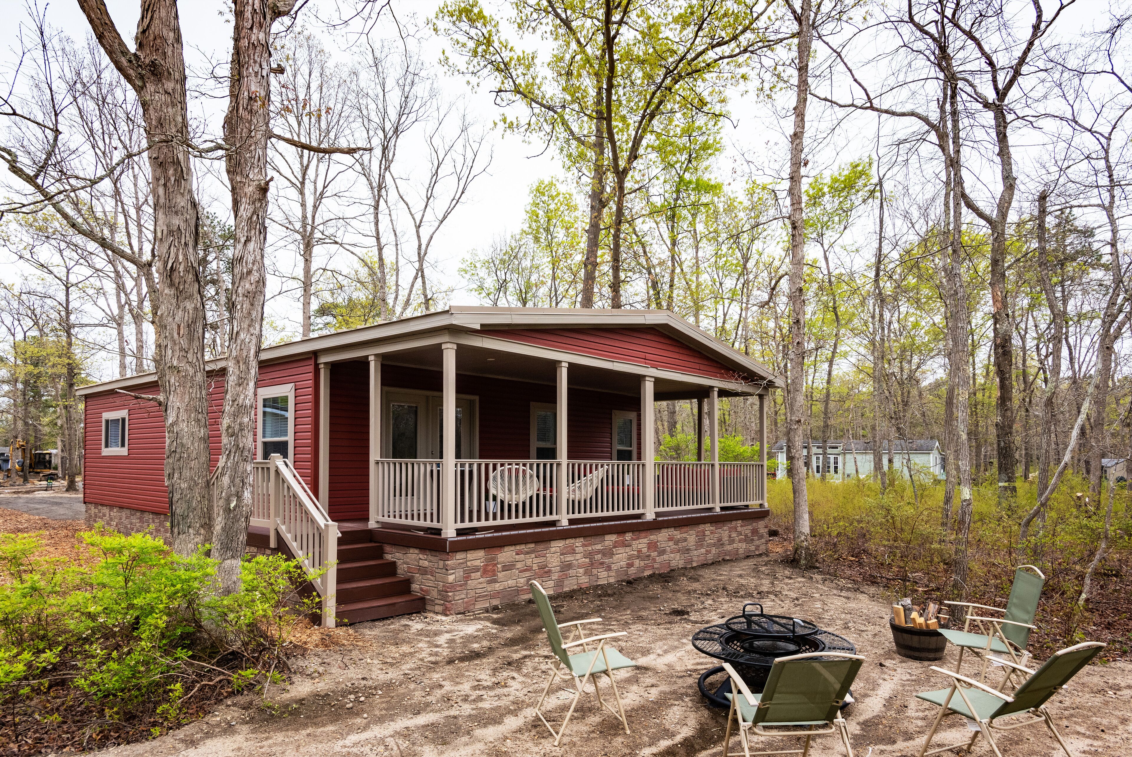 A small cabin with a porch, surrounded by trees and a dirt ground.