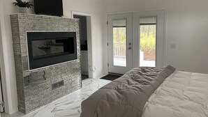 Un dormitorio con una cama grande, un televisor montado en una pared de ladrillo y una puerta que da a un balcón.