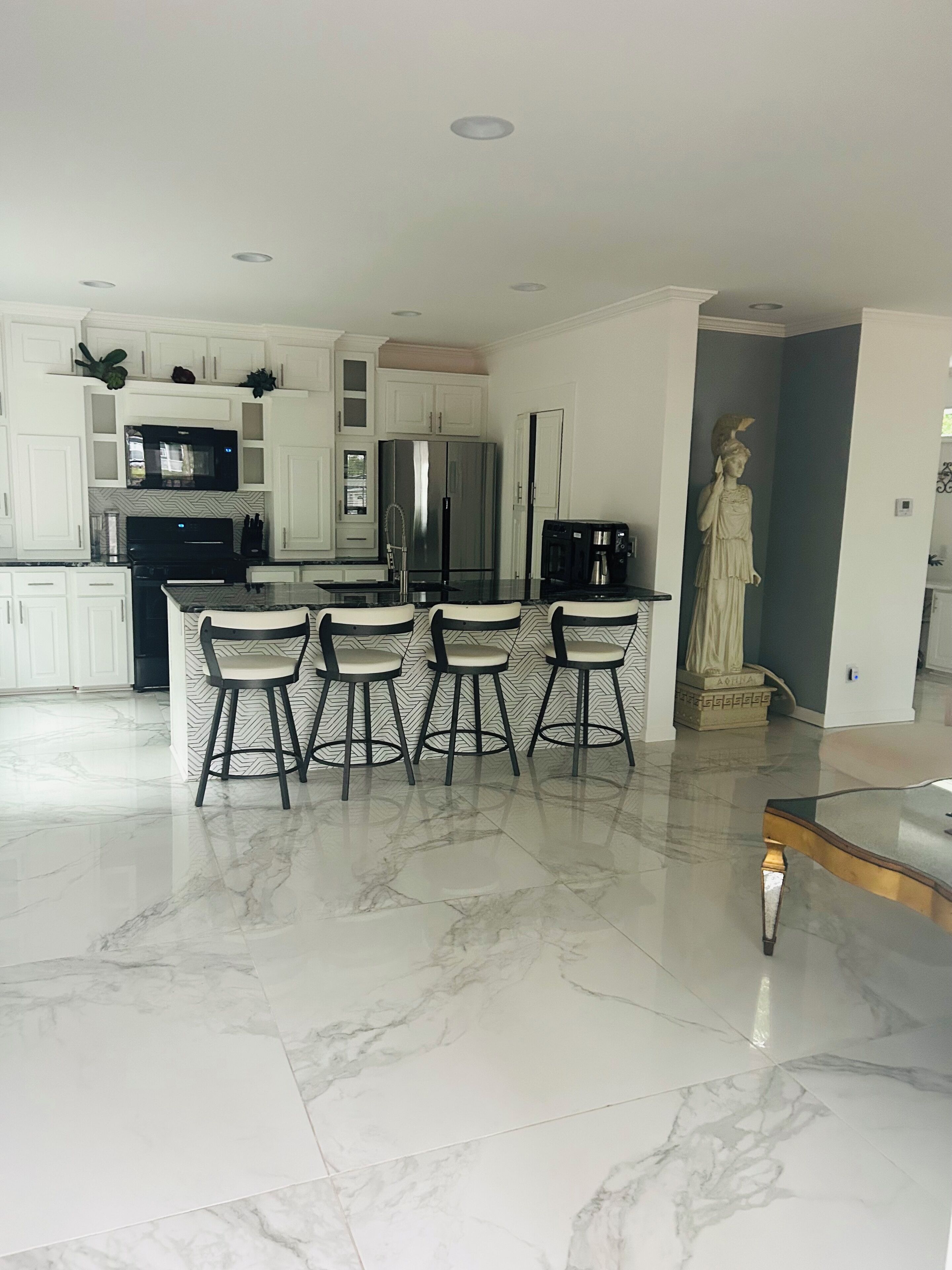 Una cocina moderna con armarios blancos, un refrigerador de acero inoxidable, un microondas negro y piso de mármol.