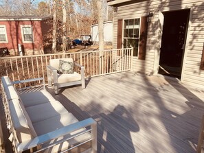 A wooden deck with a white chair and a bench, a small building with a window, and a vehicle parked in the background. - Swan Lake Resort Rentals (Absecon)