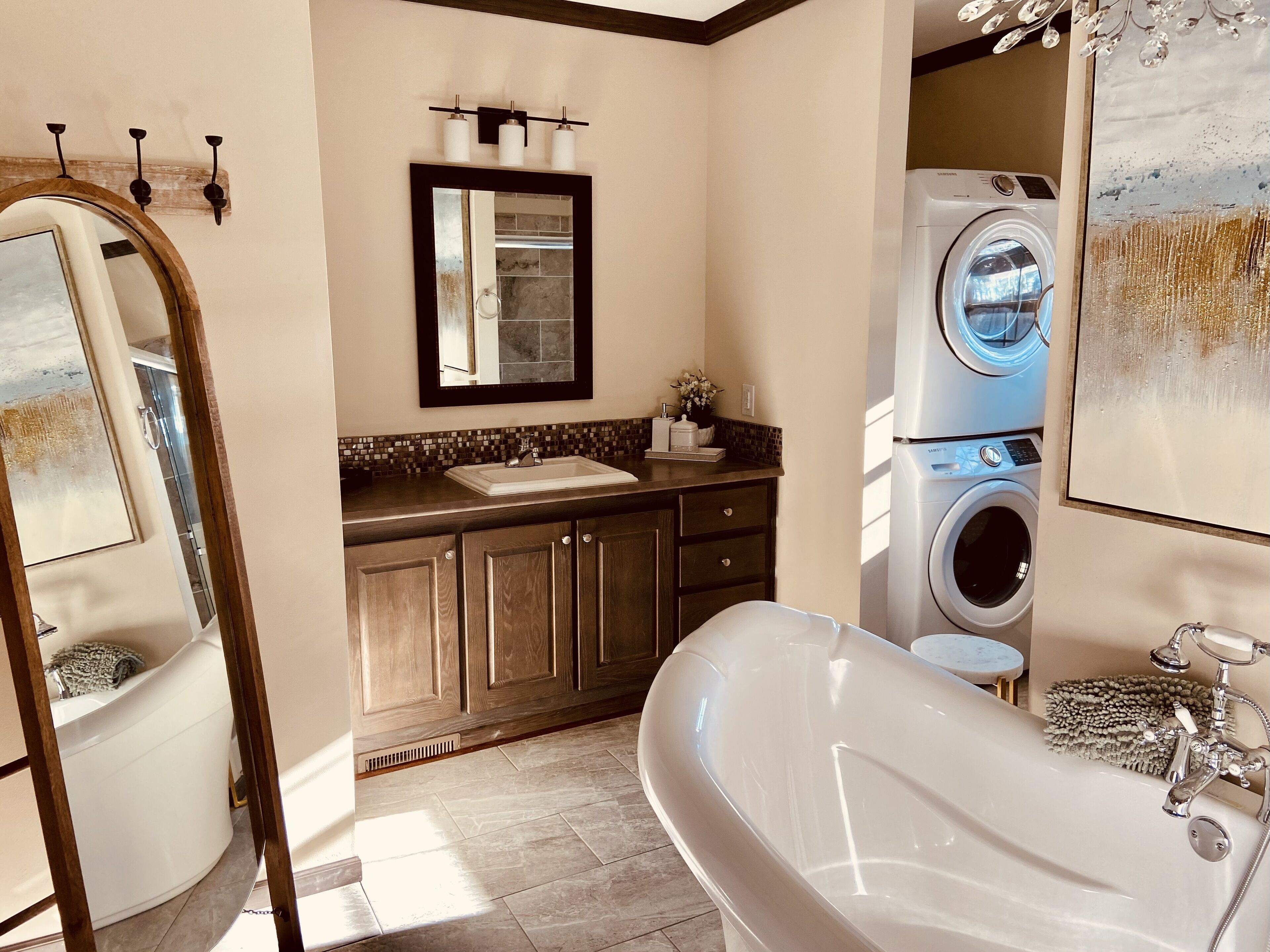 A bathroom with a freestanding bathtub, a sink with a mirror above it, a washing machine, and a tiled floor.