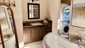 A bathroom with a freestanding bathtub, a sink with a mirror above it, a washing machine, and a tiled floor.