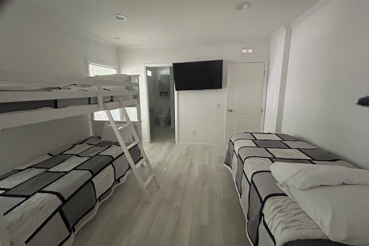 A room with bunk beds, a television on the wall, and a door leading to a bathroom.