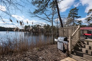A lakeside deck with a grill and steps leading to a red-roofed building. - Swan Lake Resort Rentals (Absecon)