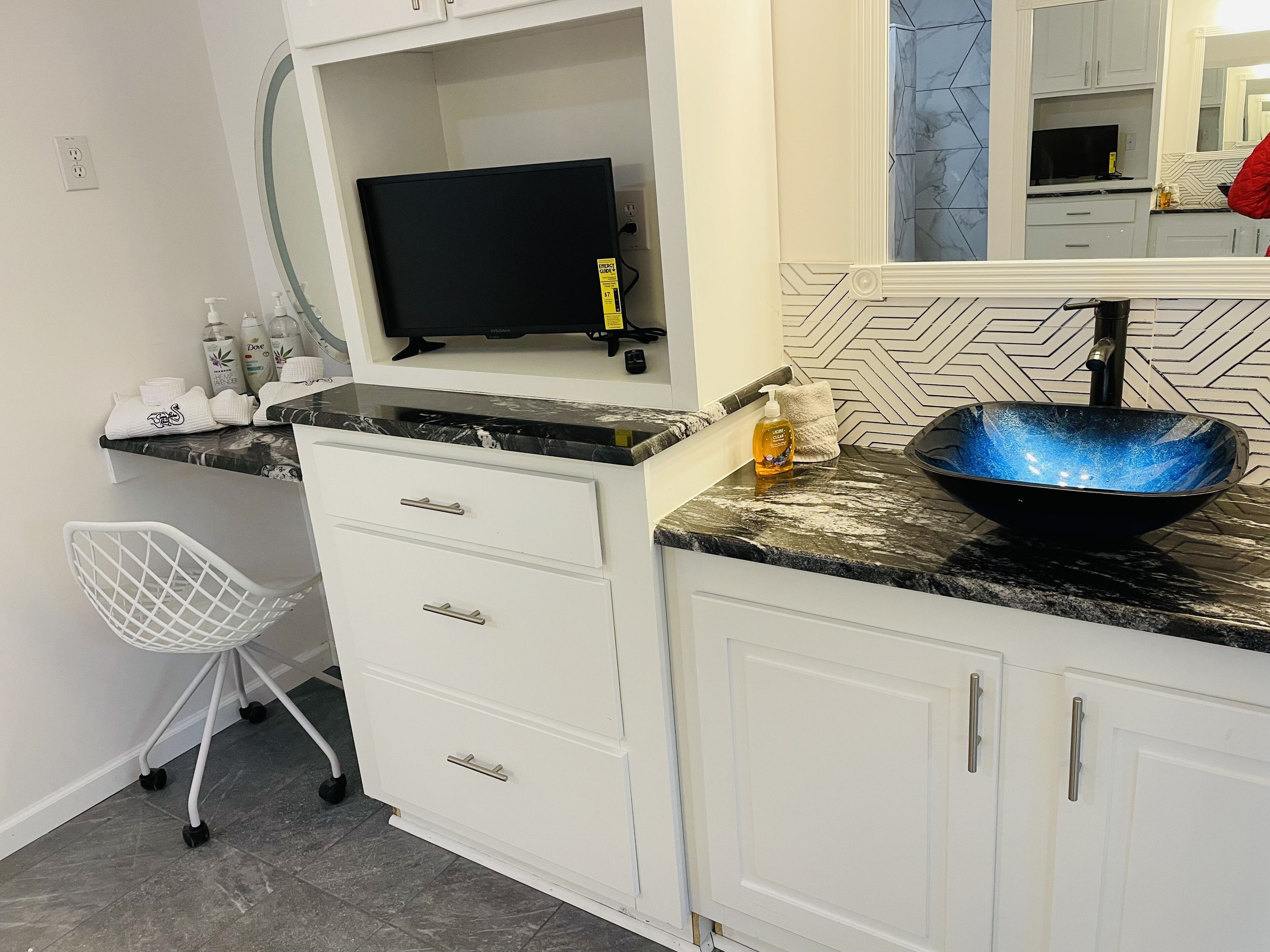 Een badkamer met een zwart wastafel, witte kastjes, een witte stoel en een spiegel.