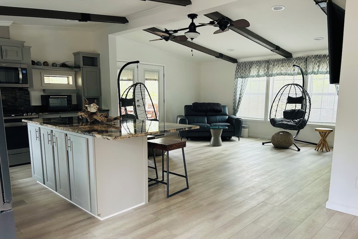 A modern kitchen with a central island, a dining area with a sofa and coffee table, and a living room with a hanging chair.