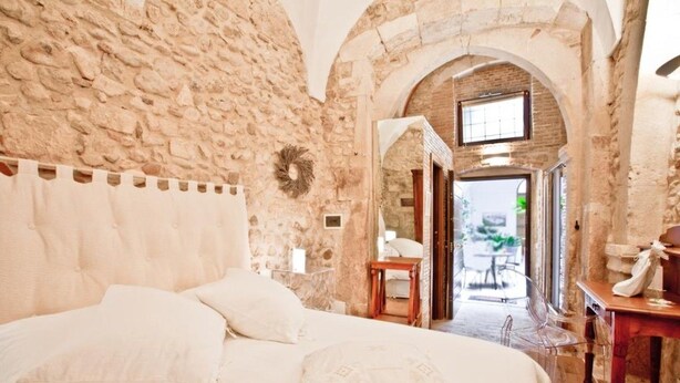 A bedroom with a stone wall, a bed with white linens, and an arched doorway leading to a balcony. - B&B Il Marchese Del Grillo (Sulmona)