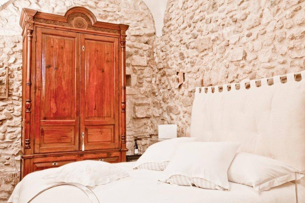 Un dormitorio con pared de piedra, un armario de madera y una cama con ropa de cama blanca.