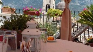 An outdoor dining area with a table set for two, overlooking a mountainous landscape with a church tower. - B&B Il Marchese Del Grillo (Sulmona)