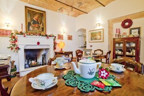 A dining area with a fireplace, a table set with tea cups and a teapot, and a Christmas wreath on the wall. - B&B Il Marchese Del Grillo (Sulmona)