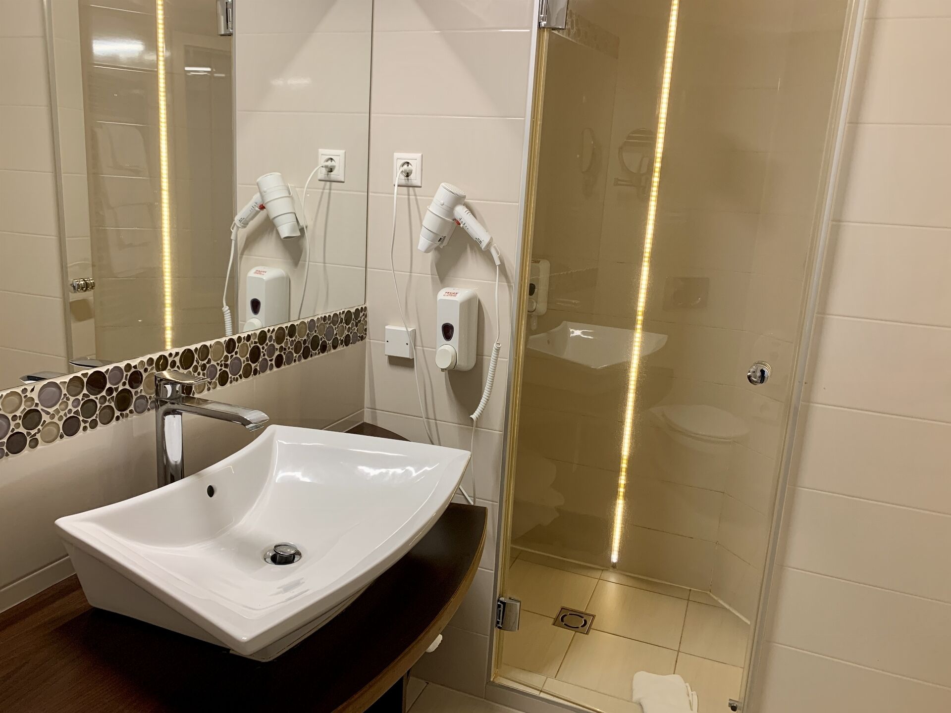A bathroom with a white sink, a mirror with a mosaic tile border, and a glass shower enclosure.