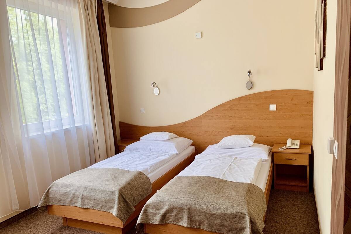 Habitación de hotel con dos camas individuales, cabecera de madera, teléfono en la mesita de noche y ventana con cortinas.