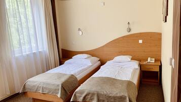 A hotel room with two single beds, a wooden headboard, a bedside telephone, and a window with curtains.