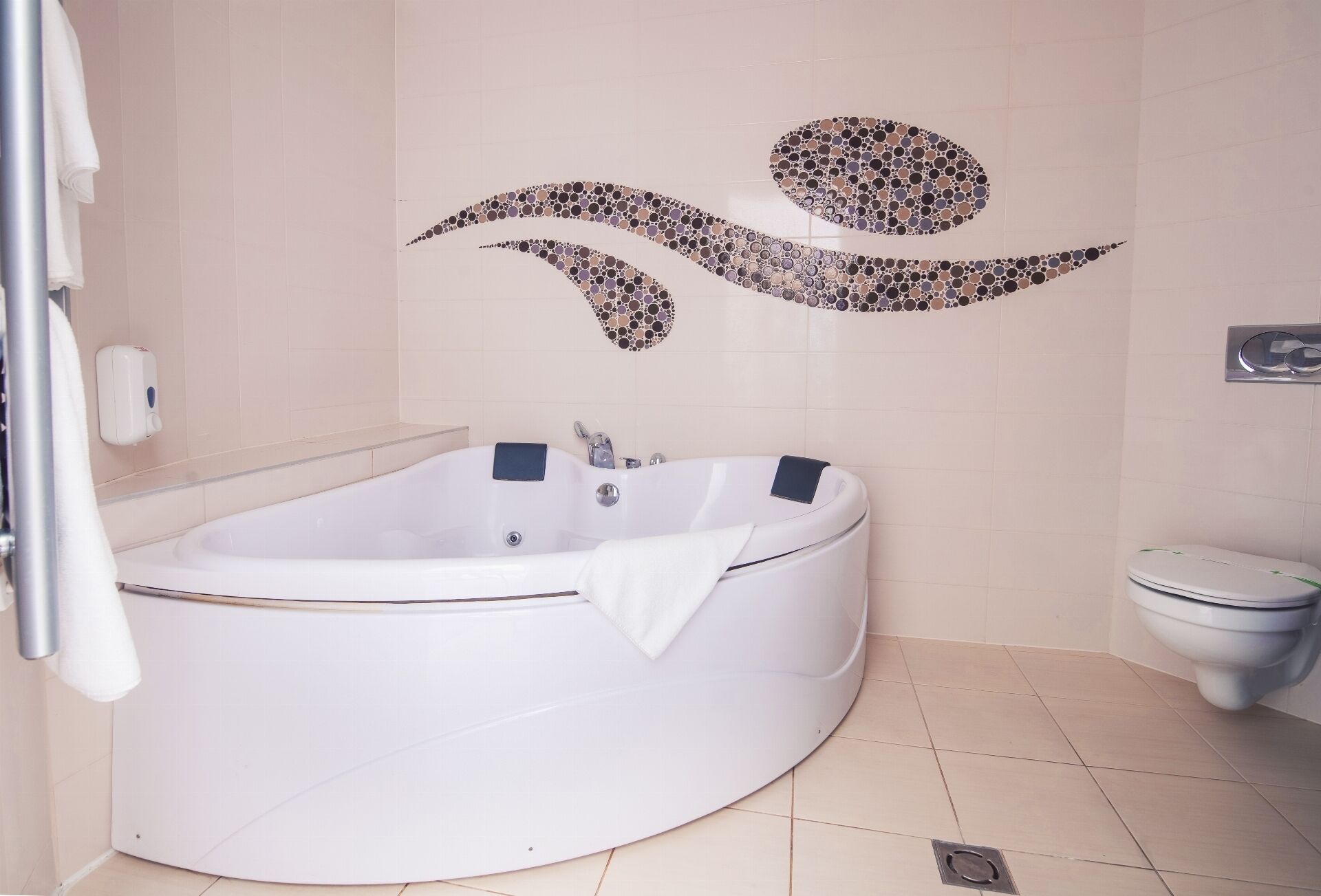 Un baño moderno con una bañera independiente, un inodoro y un dispensador de jabón para manos en la pared.