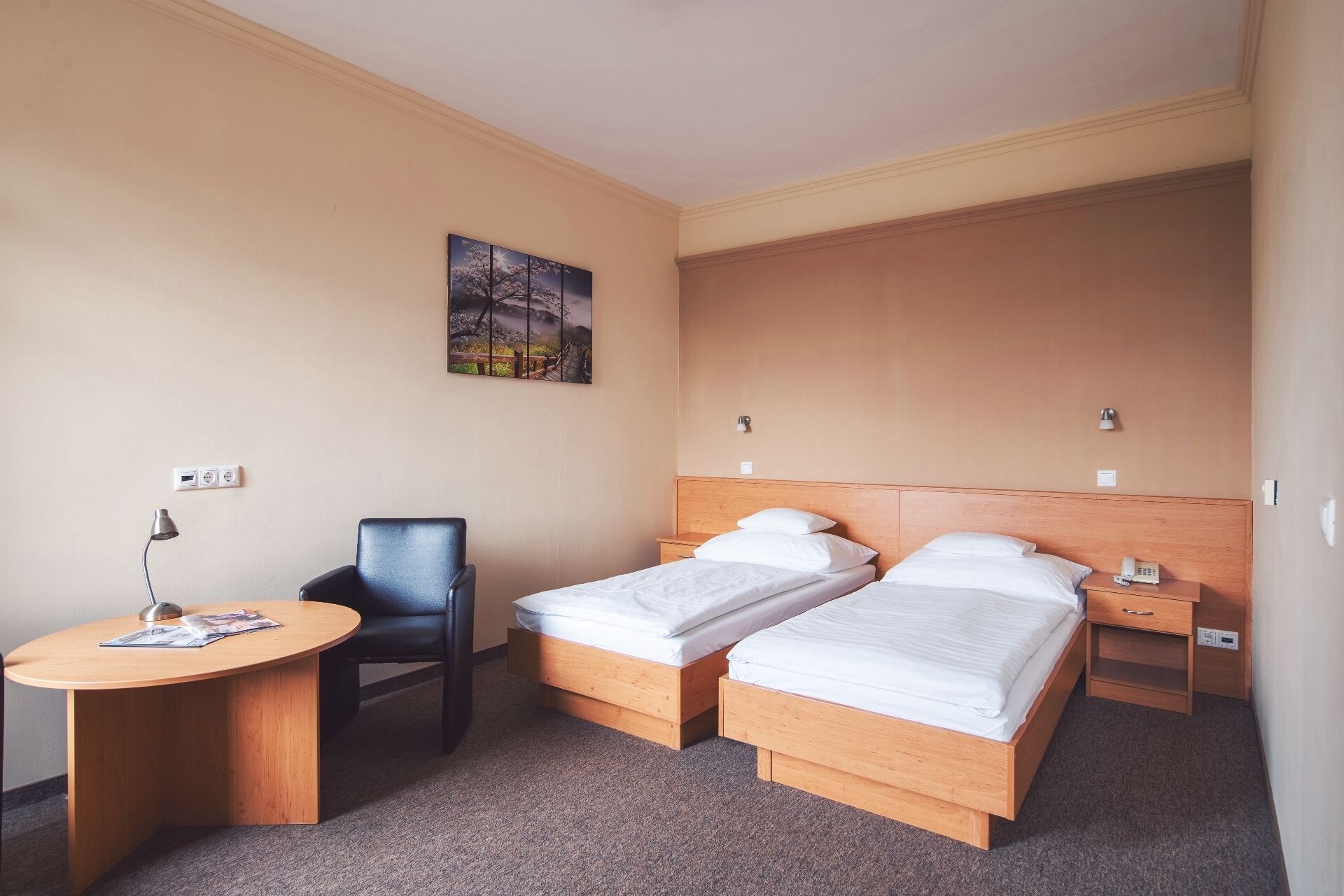 Habitación de hotel con dos camas individuales, un escritorio con silla, una mesita y un cuadro en la pared.