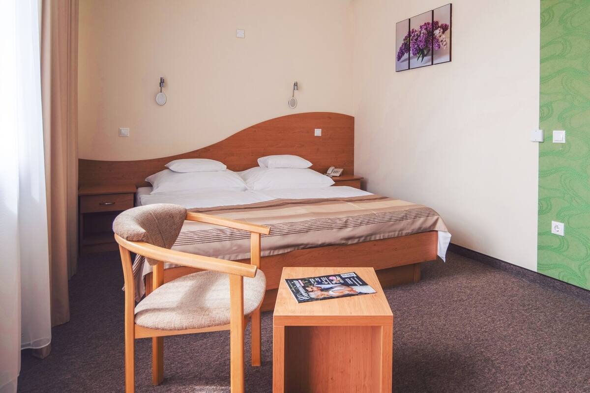 Una habitación de hotel con una cama, una silla de madera, una mesita pequeña y un teléfono instalado en la pared.