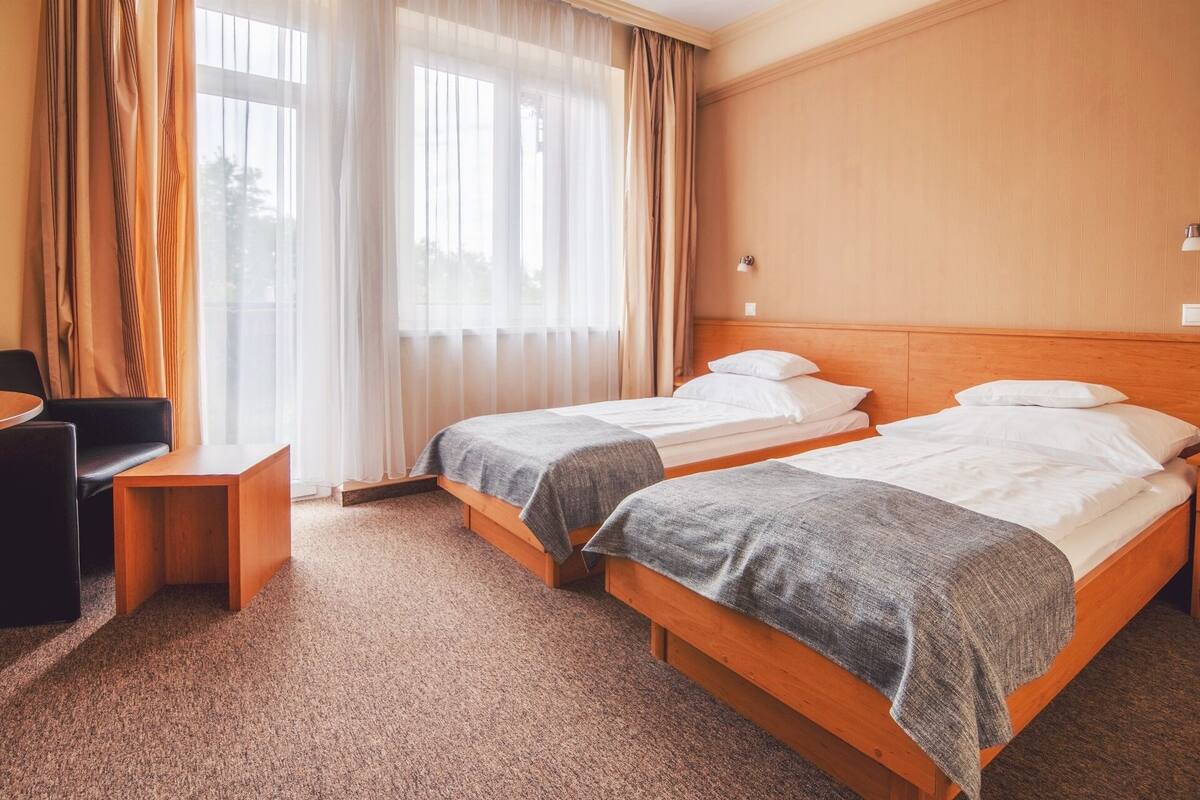 Habitación de hotel con dos camas individuales, cabecera de madera, una mesita de madera y una silla.