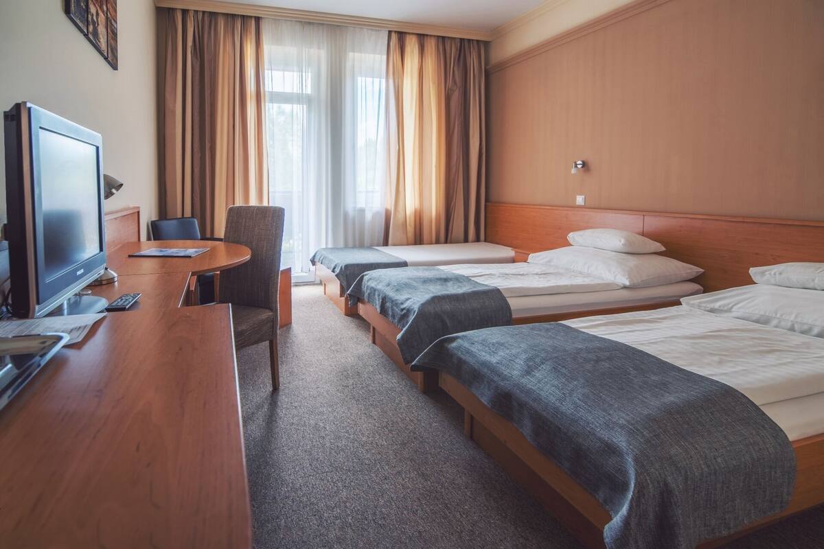 Una habitación de hotel con televisión, escritorio, silla y tres camas.