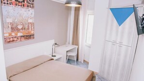 A small, neatly arranged room with a bed, a desk, and a chair. There is a window with curtains, a wall-mounted TV, and a poster on the wall. - Piccolo Sogno Inn (Pompei)