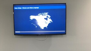 Un téléviseur à écran plat fixé au mur, au-dessus d’un meuble noir contenant un four à micro-ondes et un lave-vaisselle.