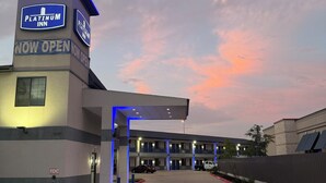 Un hôtel Platinum Inn avec une enseigne indiquant « OUVERT MAINTENANT », une entrée abritée et un parking.