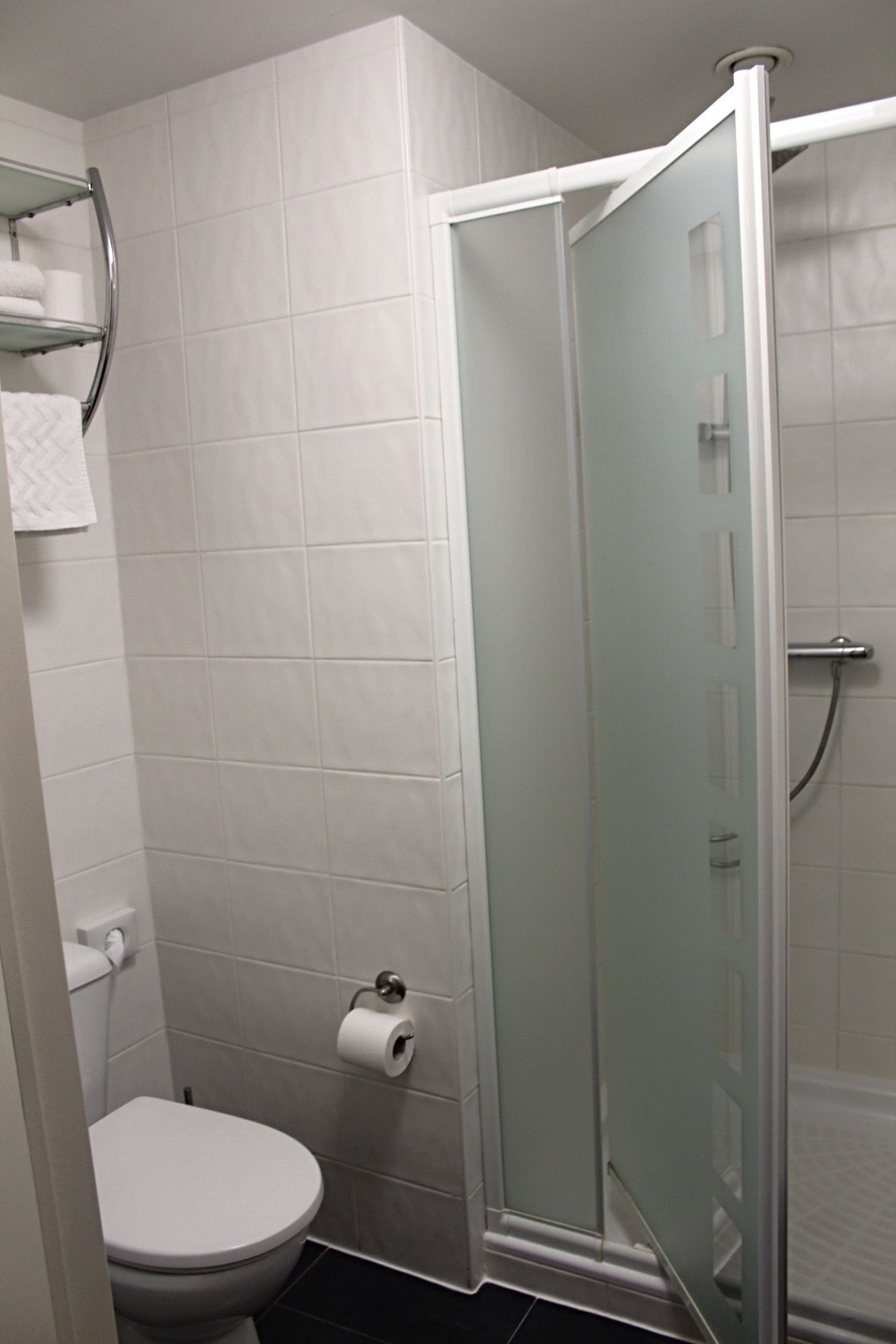Un baño con inodoro, cabina de ducha de vidrio y perchero para toallas.