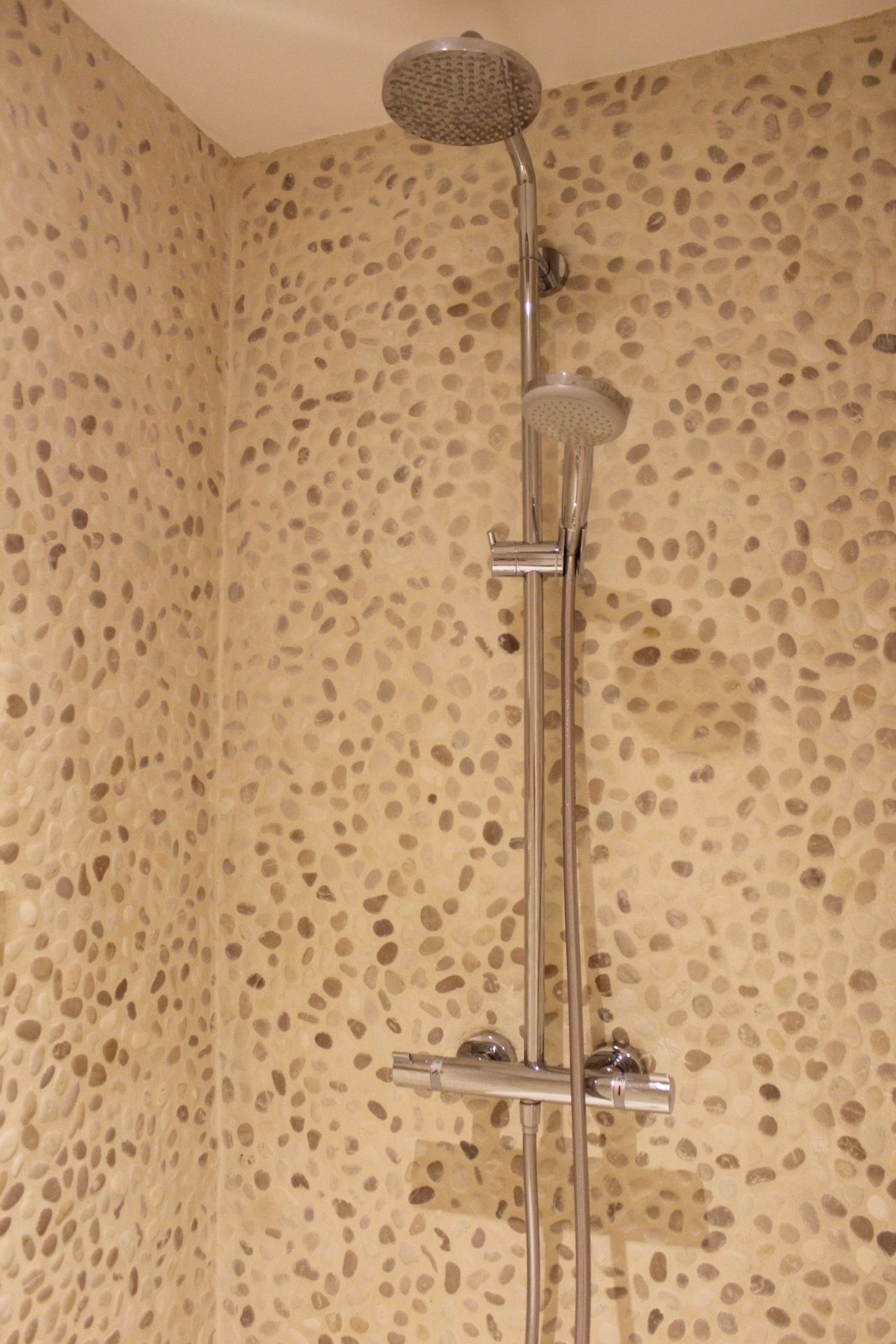 A shower with a handheld showerhead and a wall-mounted control panel.