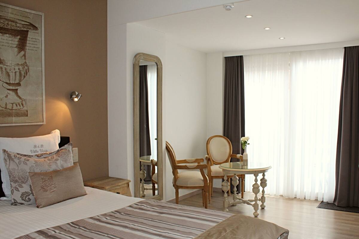 Una habitación de hotel con cama, escritorio, silla, espejo y ventana con cortinas.