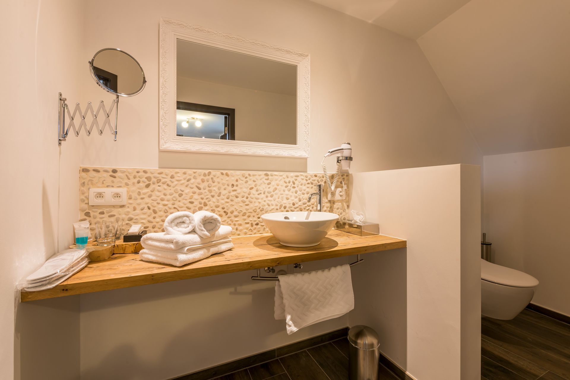 Un baño con tocador de madera, lavamanos blanco, espejo y retrete.
