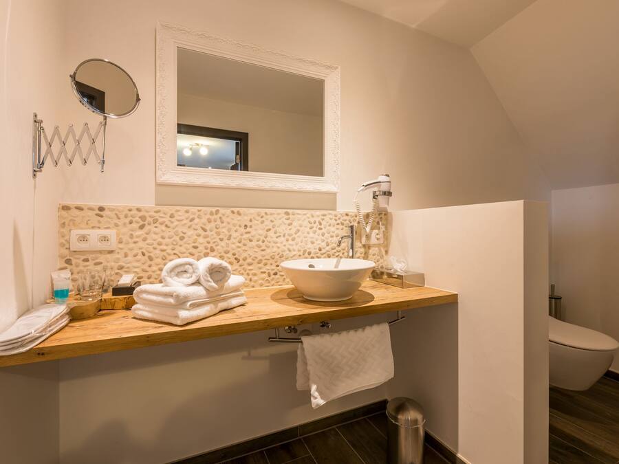 Un baño con tocador de madera, lavamanos blanco, espejo y retrete.