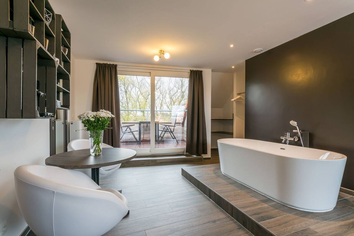 Un baño moderno con una bañera independiente, una mesa redonda con un florero y vistas a un balcón con mobiliario exterior.