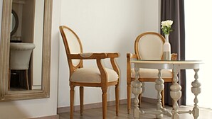Um quarto com duas cadeiras de madeira, uma mesa redonda e um espelho grande na parede.