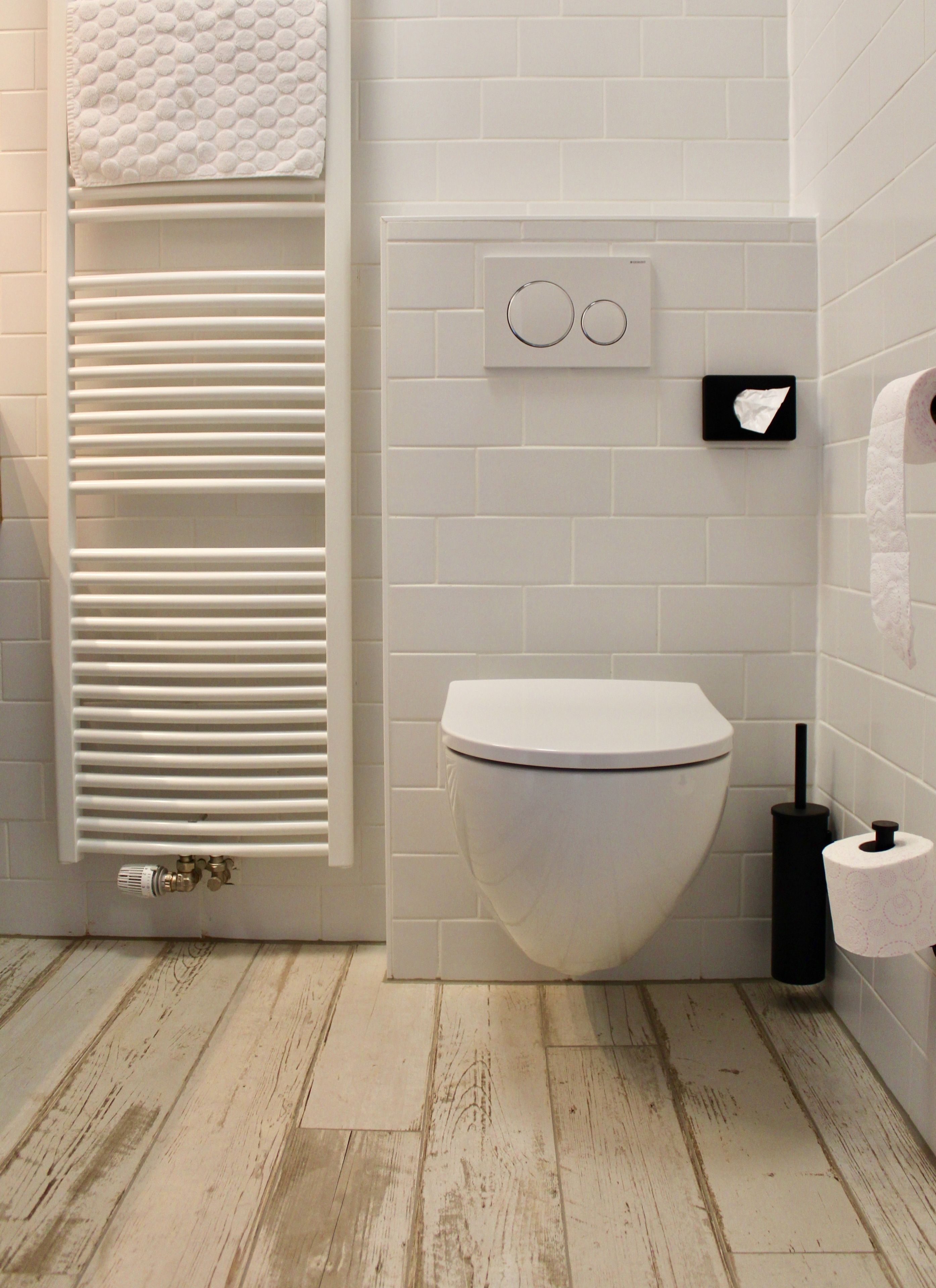 Un baño con inodoro blanco, un perchero con toalla blanca, dispensador de papel higiénico y un radiador.