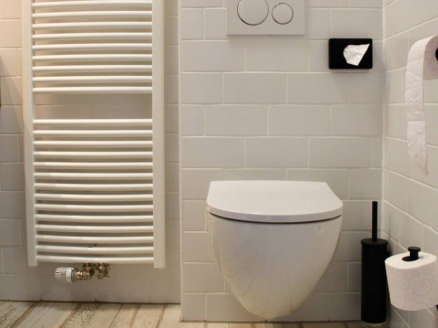 Un baño con inodoro blanco, un perchero con toalla blanca, dispensador de papel higiénico y un radiador.