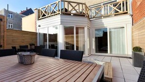 Um espaço de pátio com mesa e cadeiras de madeira, um braseiro e uma porta de vidro que dá para um espaço coberto ao ar livre.