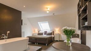 Quarto moderno com claraboia, uma cama grande, toucador e mesa redonda com um vaso de flores.