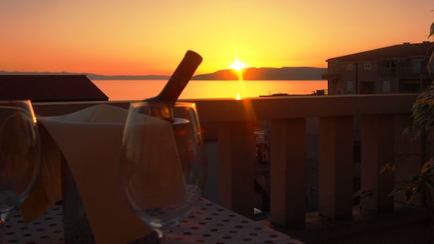 A table with a glass and a bottle, overlooking a sunset over water. - Apartments Dany (Makarska)