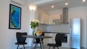 A modern kitchen with white cabinets, a stainless steel refrigerator, and a dining area with two chairs and a table. - Apartments Dany (Makarska)