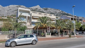 A modern building with balconies, a palm tree, and a mountain in the background. - Apartments Dany (Makarska)