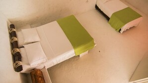 Kaksi erillistä sänkyä, joissa on valkoiset ja vihreät vuodevaatteet, puiset päätyosat ja lattialla on rustiikkinen, punottu kori.
