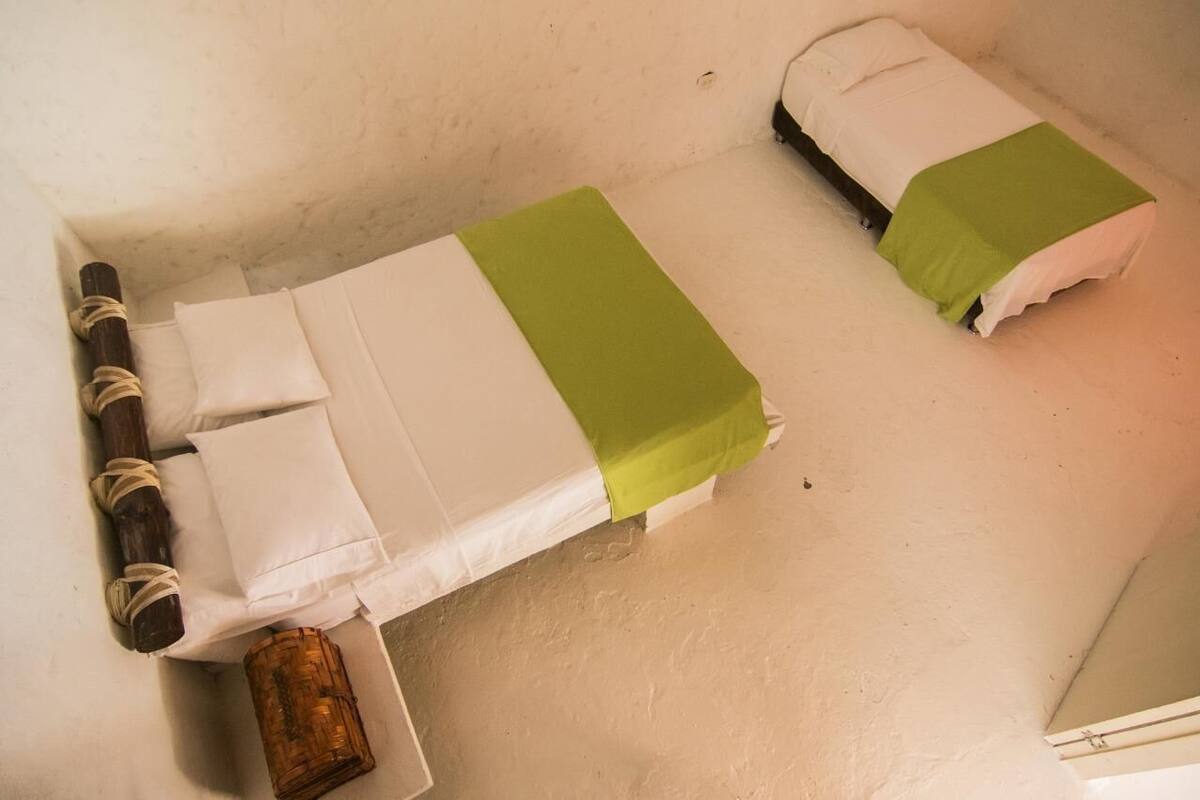 Two single beds with white and green bedding, wooden headboards, and a rustic woven basket on the floor.