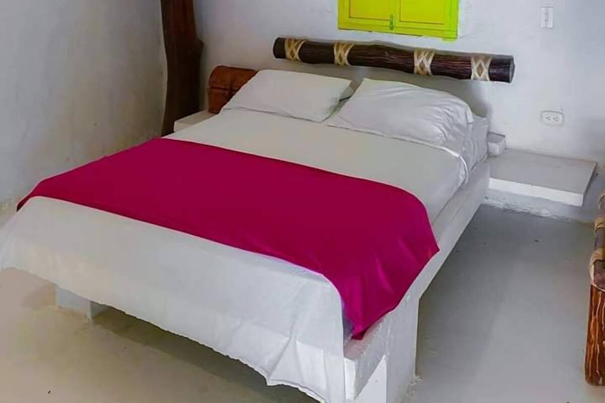 A bed with a white and pink bedspread, a wooden headboard, and a bright green window shutter.