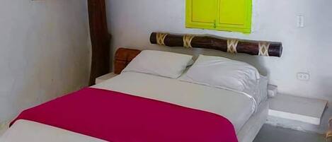 Un lit recouvert d’une couvre-lit blanche et rose, avec une tête de lit en bois et un volet de fenêtre d’un vert vif.