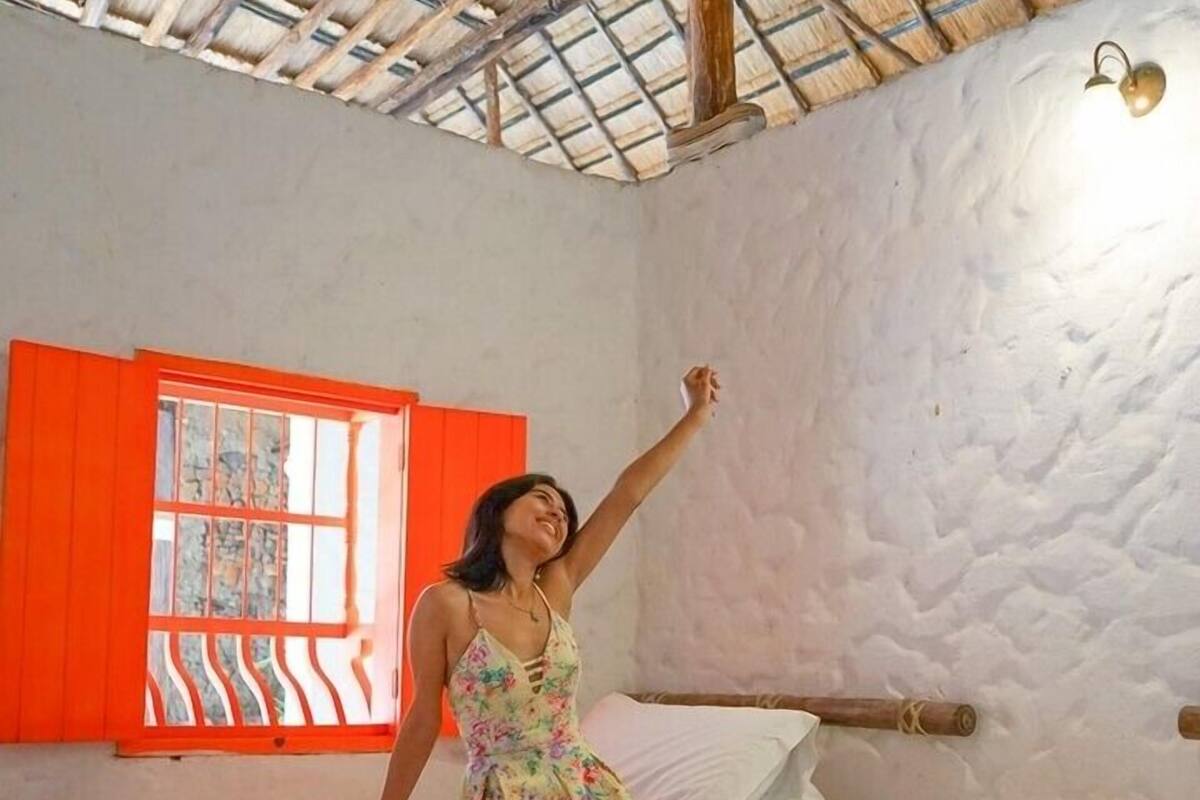 A room with two beds, a window with red shutters, and a thatched roof.